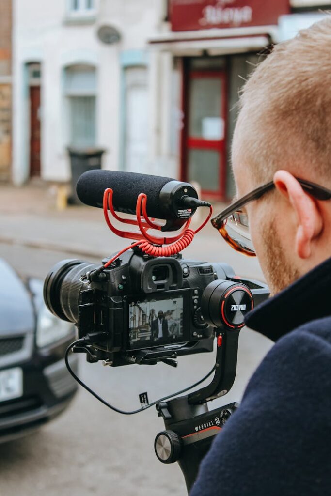 A videographer uses a camera to film a street scene, focusing with precision.