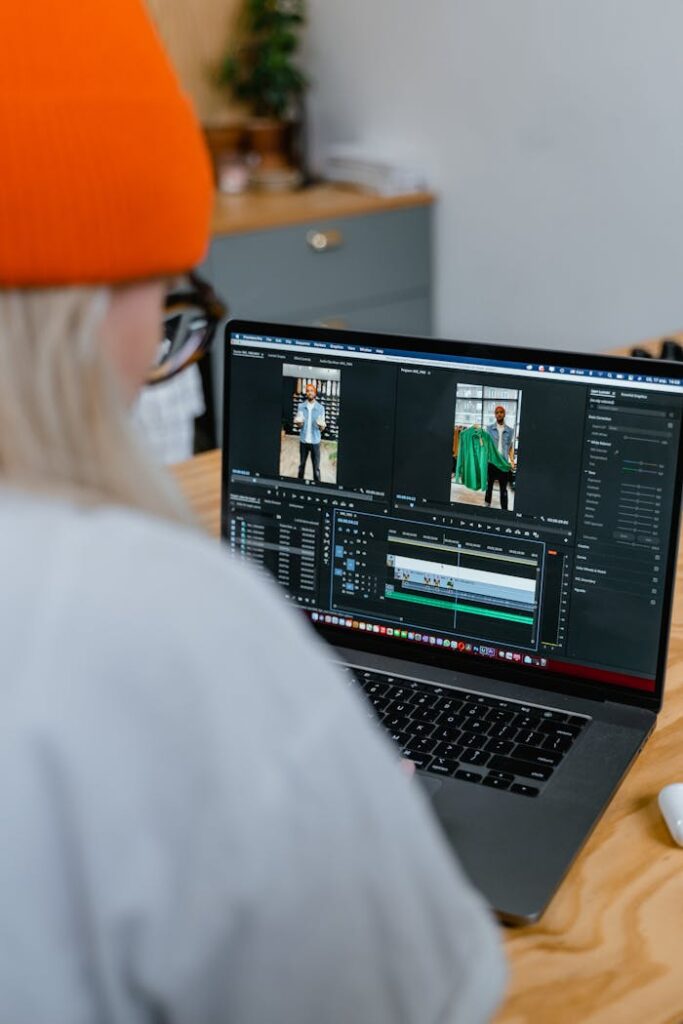 Woman focused on video editing using a laptop in a modern office setting with a bright orange hat.
