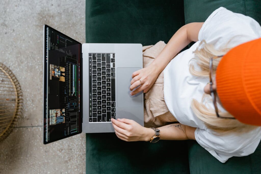 Top view of a woman editing video content on a laptop, wearing a casual outfit and orange beanie.